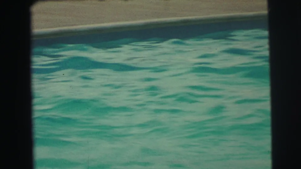 1971 8mm frame from Yellowstone, Wyoming showing the pool coping and rippling blue-green water from a fixed poolside view.