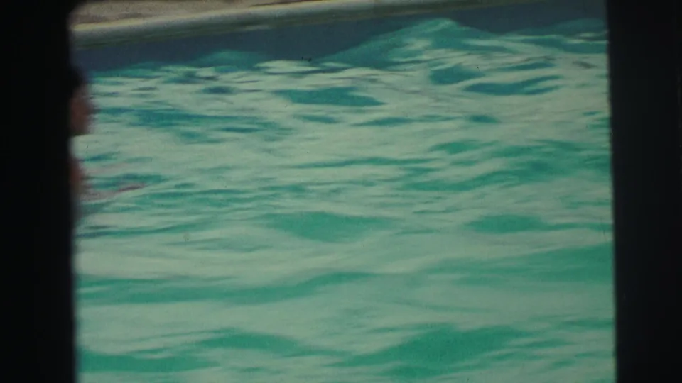 1971 Yellowstone, Wyoming home-movie frame with rippled pool water and a partly visible swimmer near the dark frame divider.