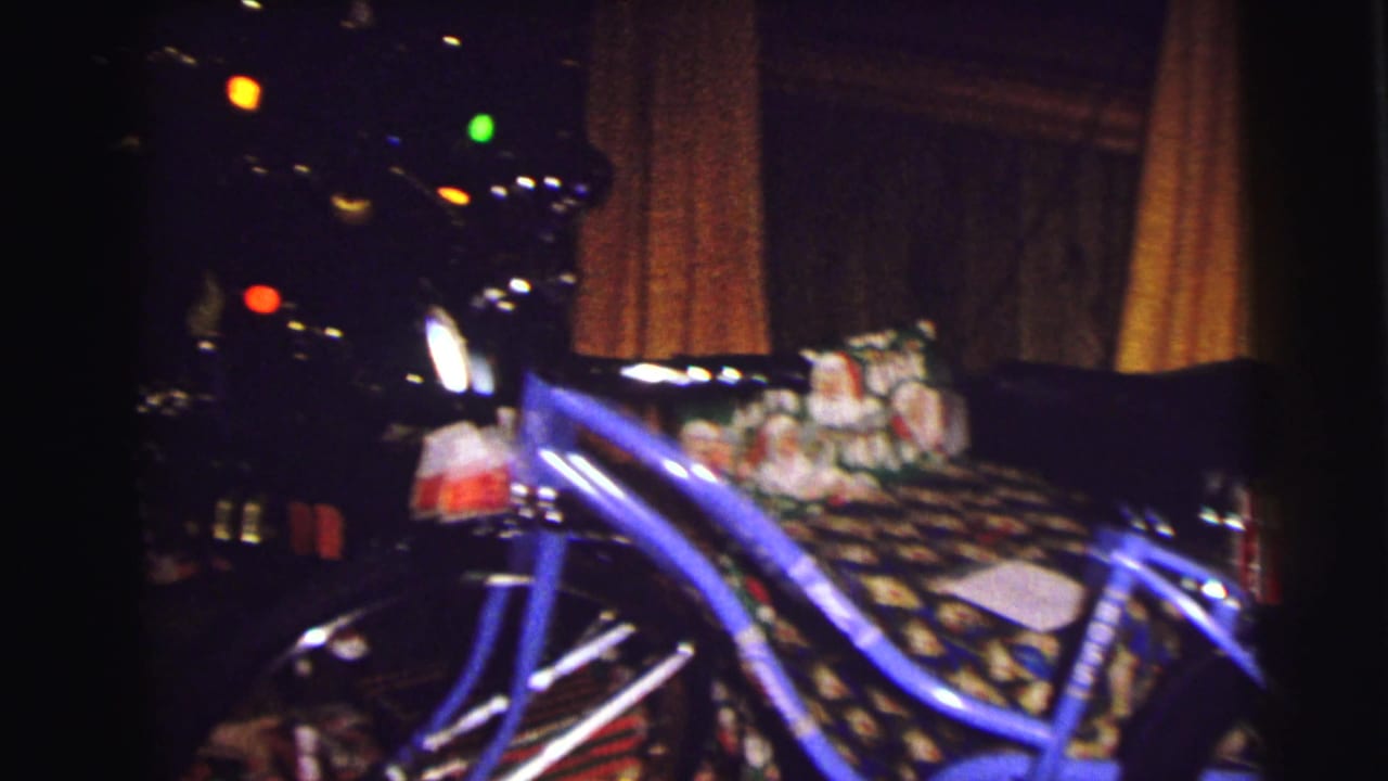 Blue bicycle and wrapped presents beside a lit Christmas tree in a dark room.