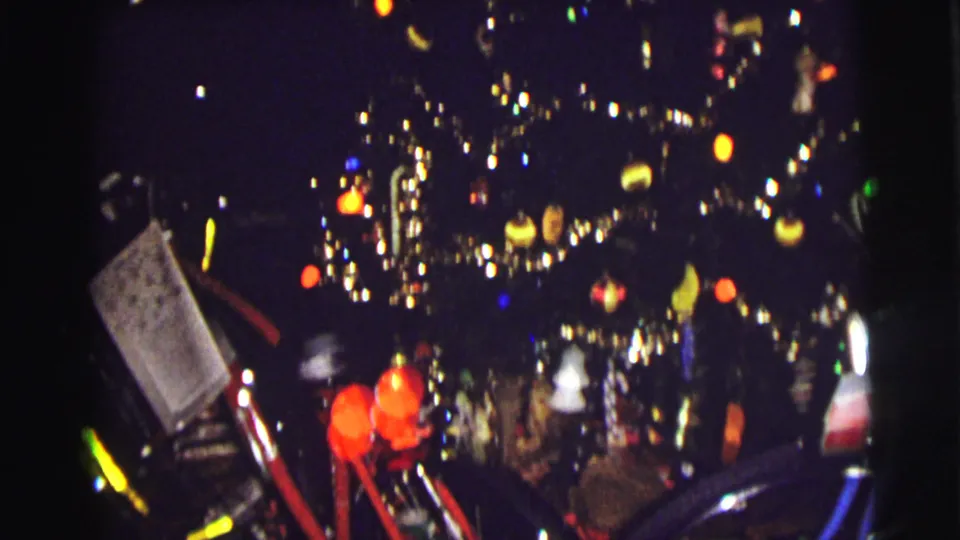 1972 East Lansing home-movie frame showing a lit Christmas tree with ornaments, tinsel, bicycles, and gifts in a dark interior.