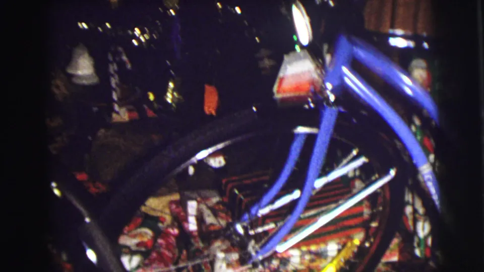 Close 1972 home-movie view of a blue bicycle under the Christmas tree in East Lansing, with lights and decorations behind it.