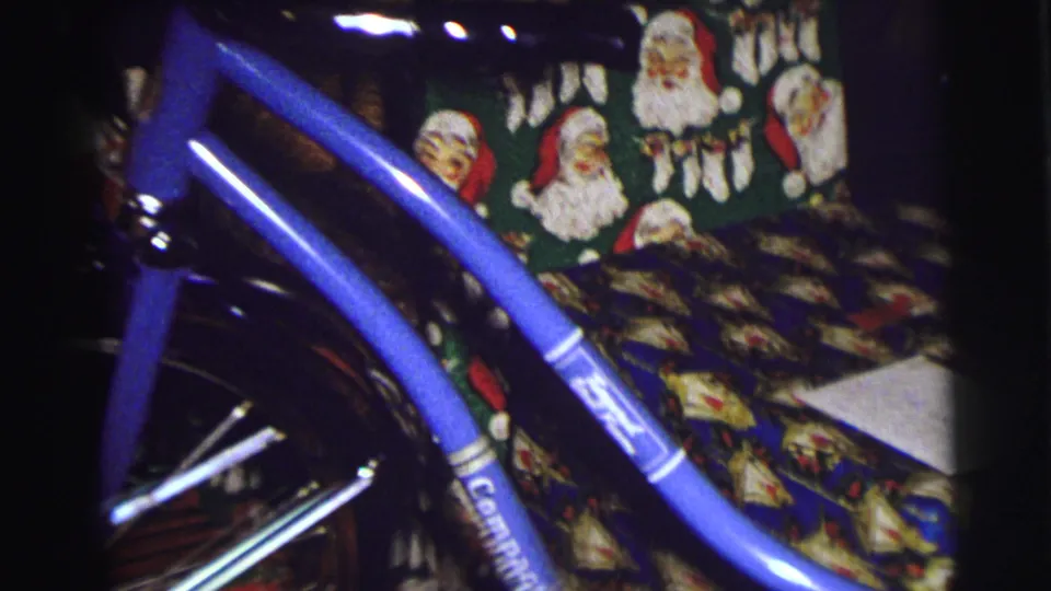 Blue bicycle framed against Santa-patterned fabric and holiday wrapping in a 1972 East Lansing Christmas home-movie scene.