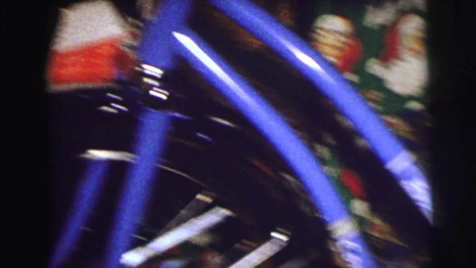Handheld 8mm frame from East Lansing showing a blue bicycle moving through blur beside Santa-patterned holiday fabric.