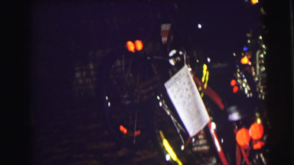 Red bicycles, a white tag, and scattered holiday lights appear in a dark 1972 East Lansing interior.