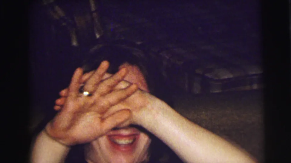 A flash-lit 1972 East Lansing frame shows the person laughing while covering most of their face with both hands.