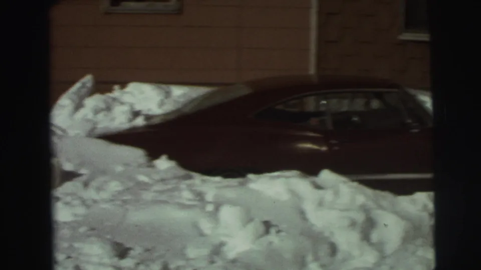 Red sedan surrounded by deep snow in a residential East Lansing winter scene from 1972.