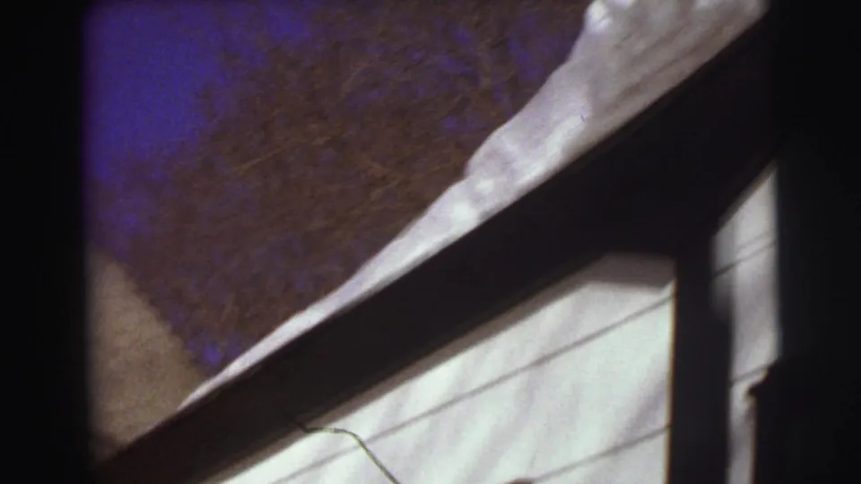 Handheld 8mm view of a snow-loaded roofline and white house siding against bare winter trees in East Lansing.
