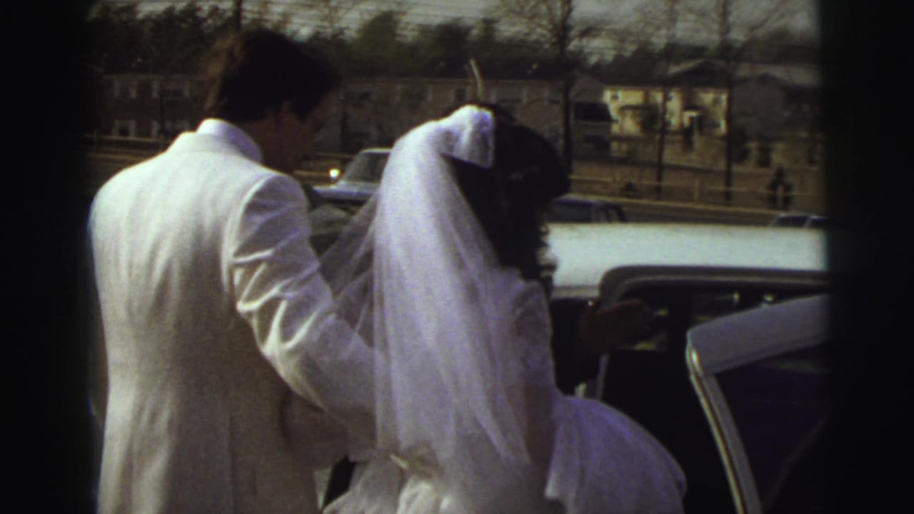 In East Lansing, Michigan in 1972, a bride in a white veil appears to hesitate beside an open car as the groom helps from behind.