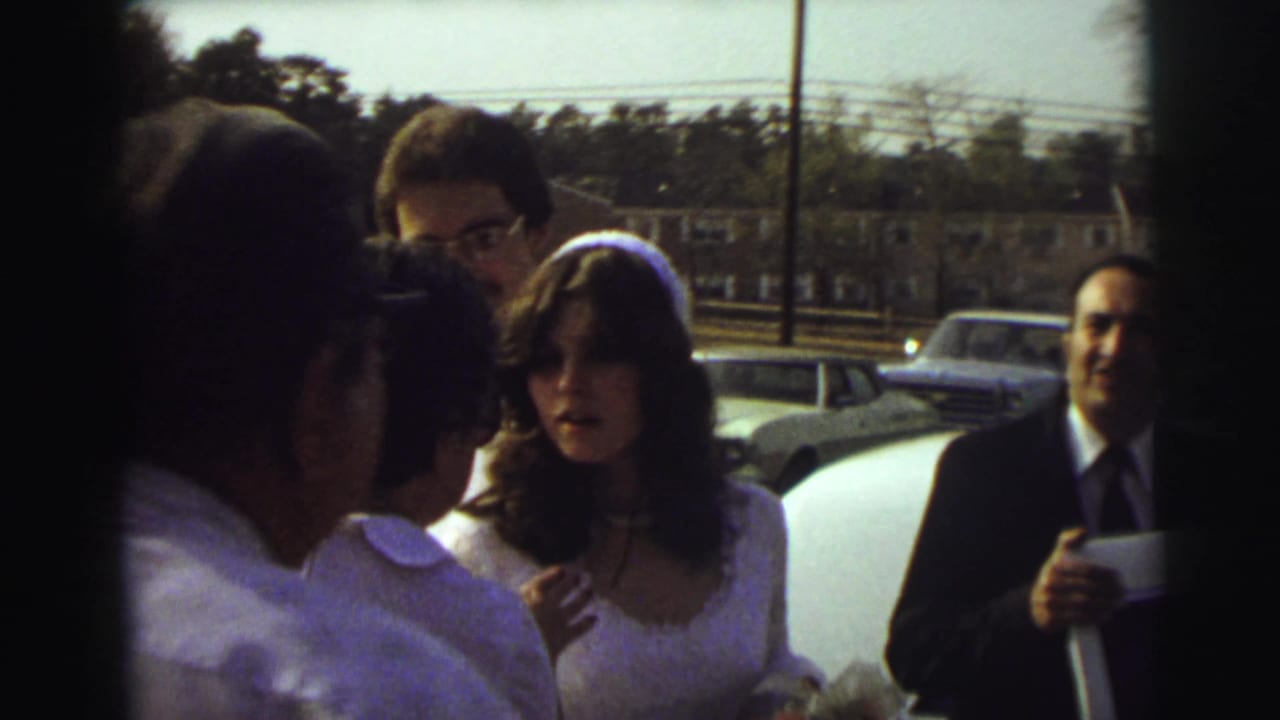 Bride and groom stand with guests beside a white limousine on a suburban roadside.