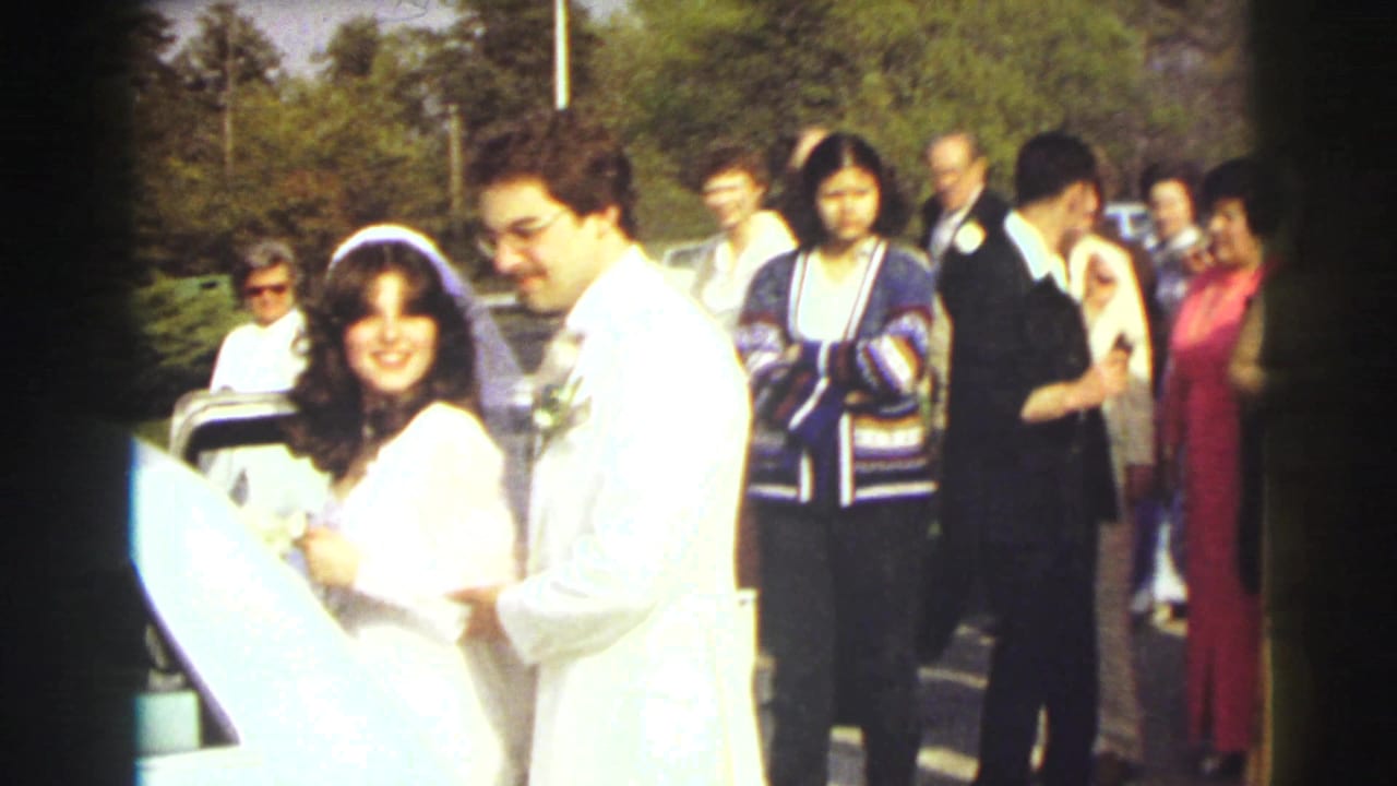 Bride and groom stand by a white limousine with wedding guests behind them.