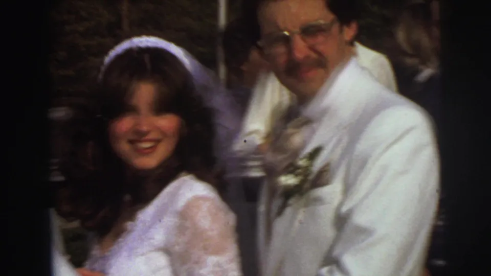 A soft, close 8mm view shows the bride in a lace dress and veil next to the groom in a white suit during the East Lansing wedding departure.