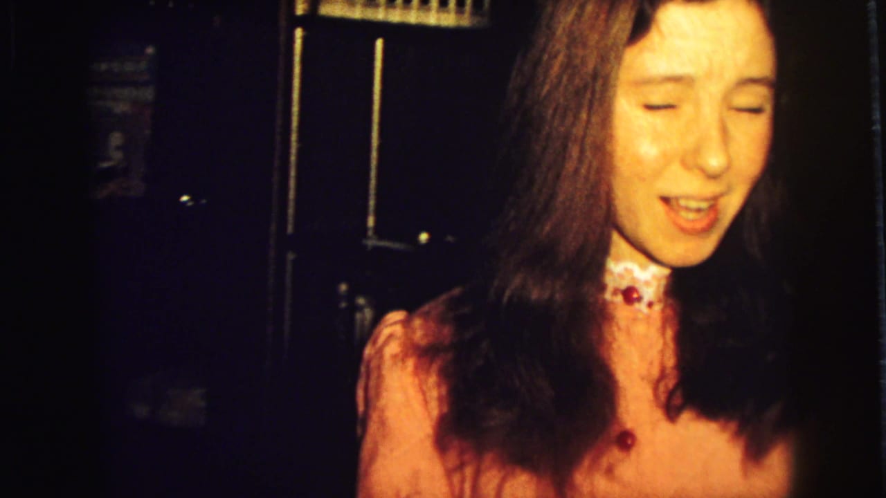 Young woman in a pink dress standing in a dim home interior.