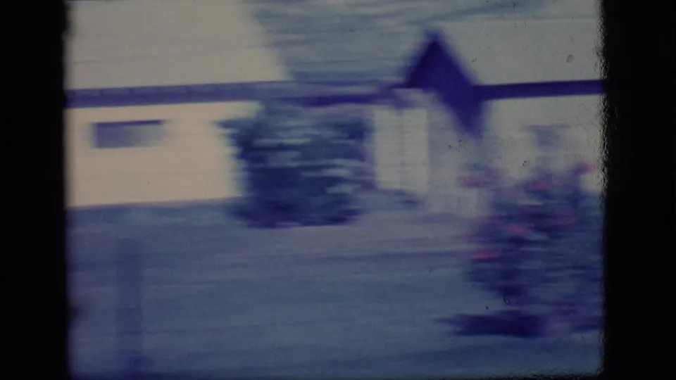 1968 Ely, Nevada residential frame with a pale house, central shrub, flowers, and strong 8mm motion blur from the passing camera.