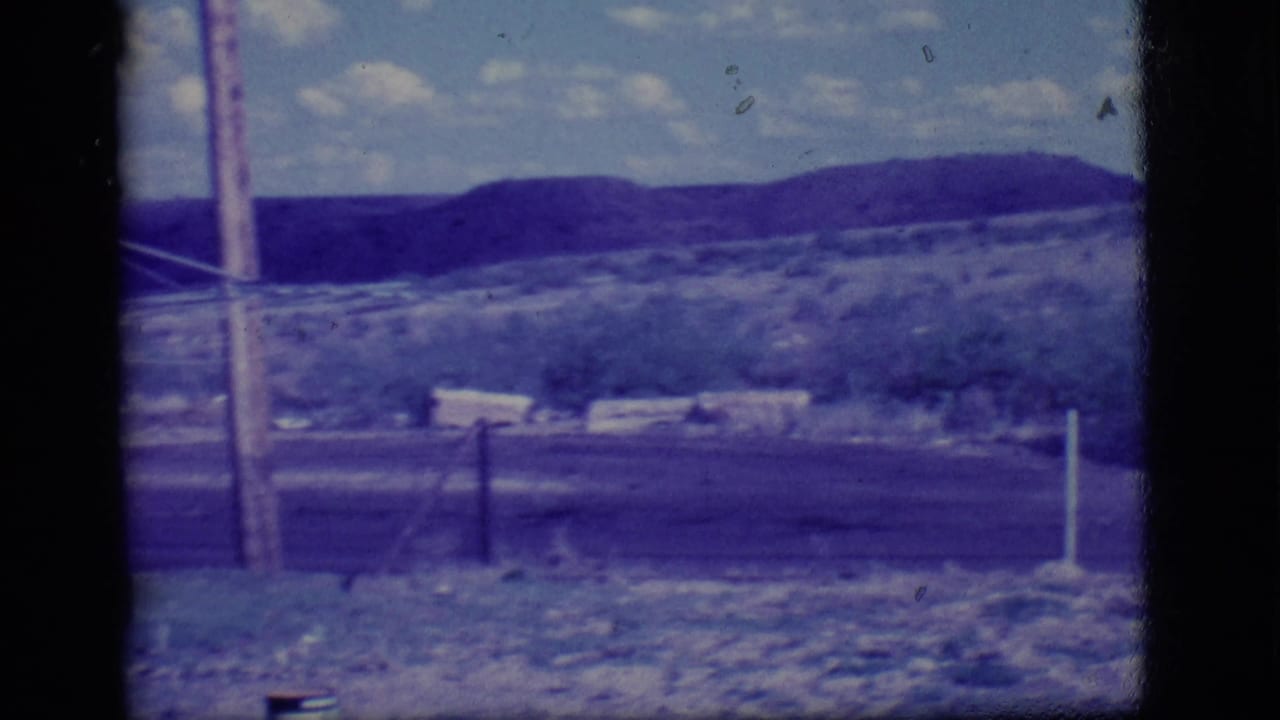 Dry rural field seen through dark window bars with utility poles and low hills beyond.