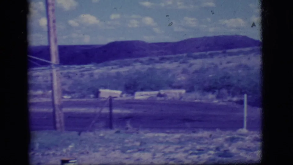 1968 Ely, Nevada home-movie frame showing a dry field, roadside posts, utility poles, and distant hills through a window frame.