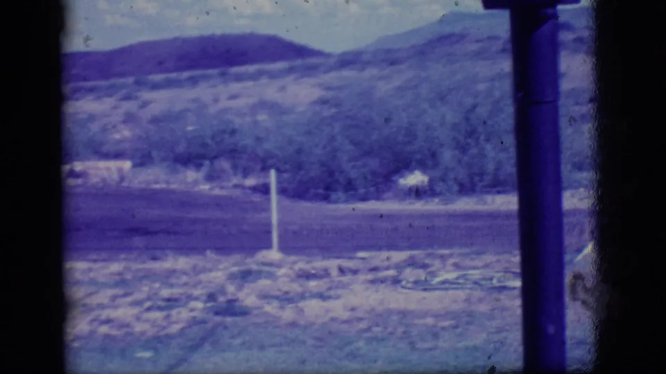 1968 Ely, Nevada frame of open roadside land with sparse brush, a white post, a utility pole, and low hills beyond.