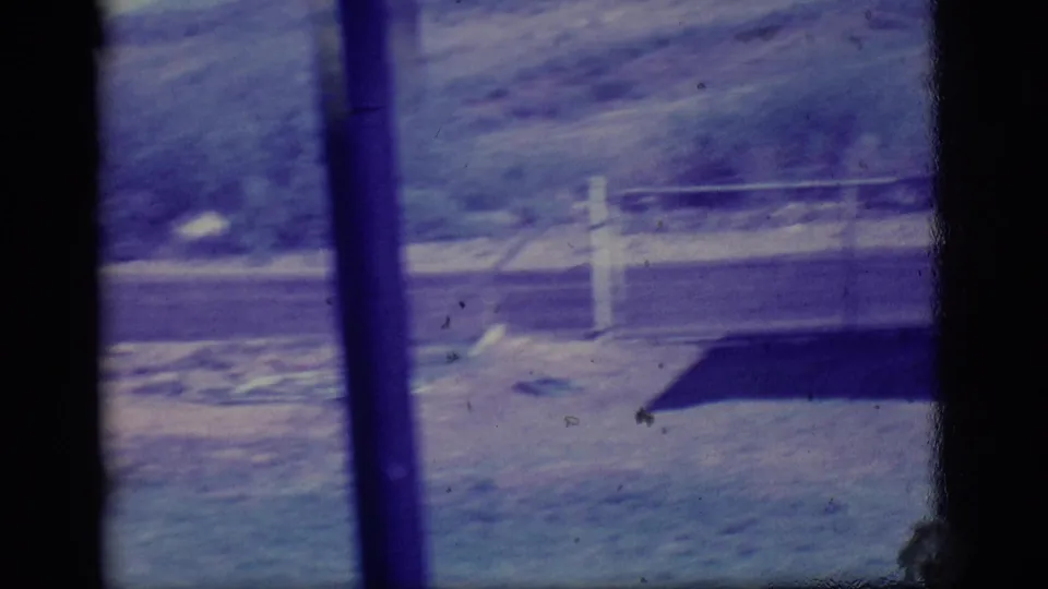 1968 Ely, Nevada frame with handheld motion blur, window bars, a roadside post, utility pole, pale field, and a dark roof edge.