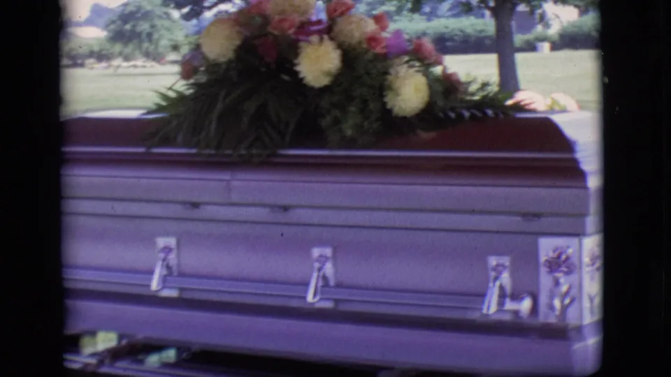 Casket with silver hardware and floral spray seen outdoors in 1966 Des Moines, Iowa home-movie footage.