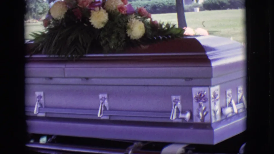 Wide 8mm frame of a casket on a hearse with flowers above it, filmed outdoors in Des Moines in 1966.