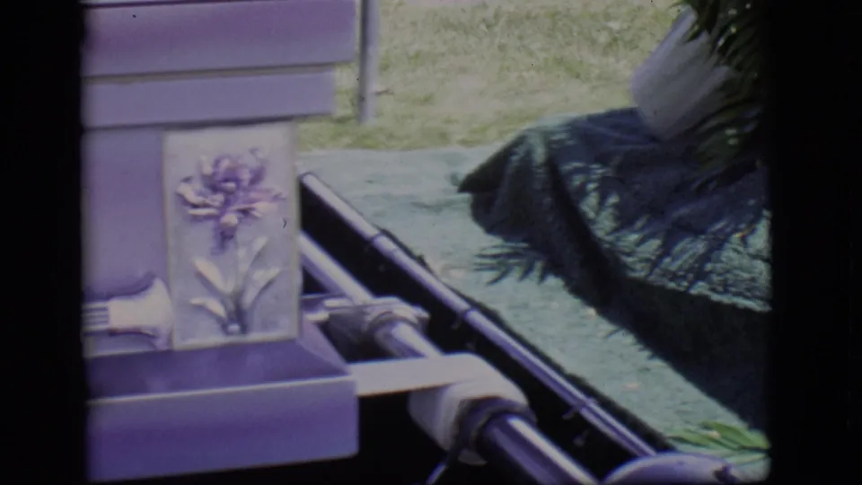 1966 Des Moines frame showing the lower corner of the lavender casket, metal carrier rails, floral ornament, and dark draped fabric nearby.