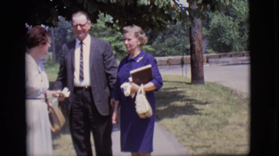 In the Des Moines 1966 clip, the group appears to chat while walking, with the woman in blue holding gloves, a book, and a woven purse.