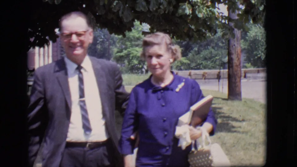 The couple appears closer to the camera in 1966 Des Moines, with the man in a suit and the woman holding a book and handbag.