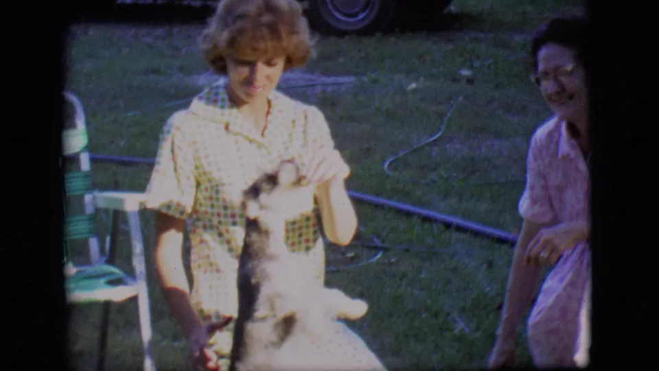 The small gray dog stands on its hind legs toward a woman in a checkered dress as another woman smiles beside her.