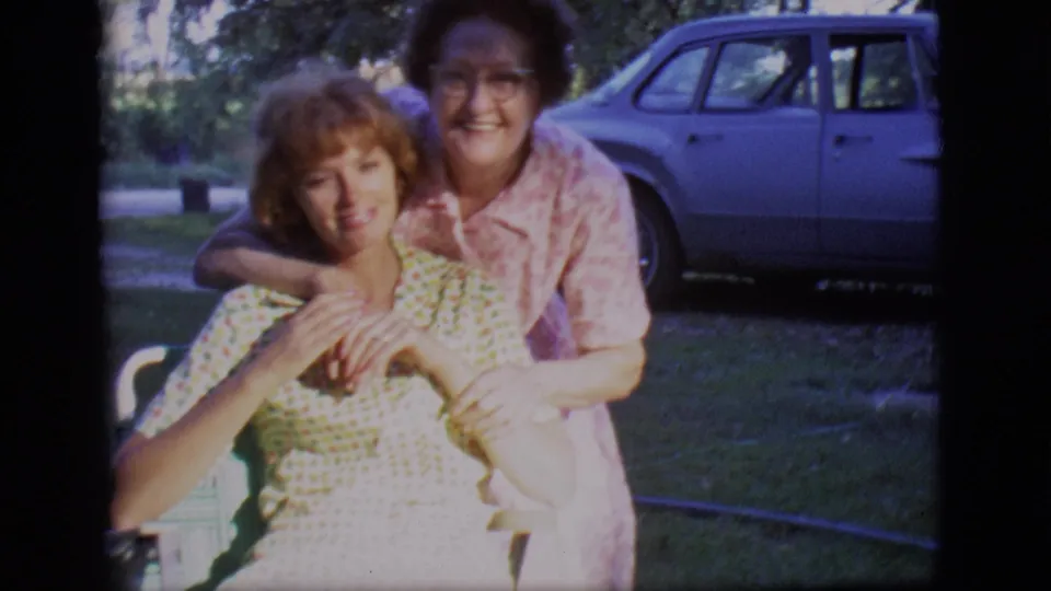 The final 1966 Des Moines frame shows two adult women smiling in a close lawn embrace, with trees and a parked 1960s sedan in the background.