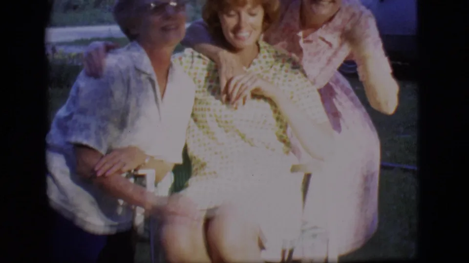 Three women remain gathered around a chair in the Des Moines backyard, with hands close together in a playful pose.
