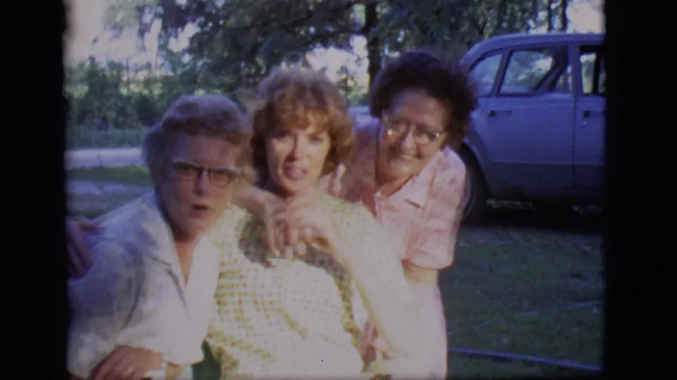 The three women face the camera in 1966 Des Moines footage, with one seated between two companions in the grass.