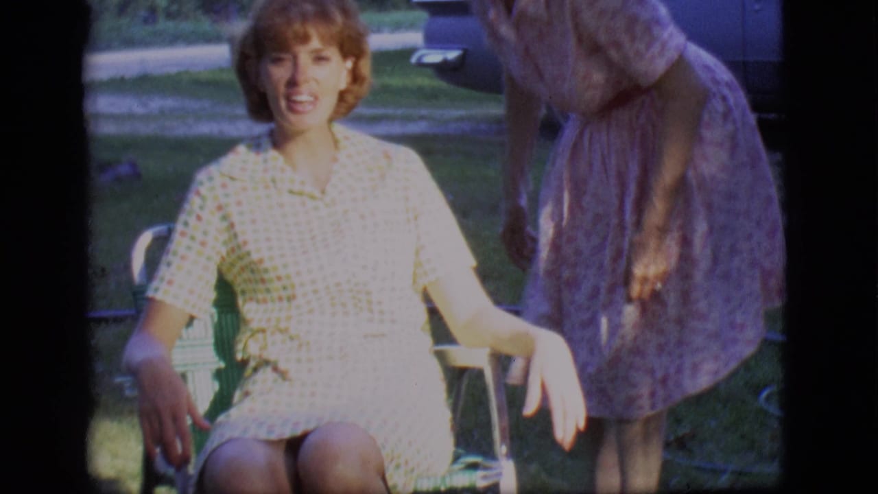 Young woman in a checkered dress sits in a lawn chair as another woman leans beside her.