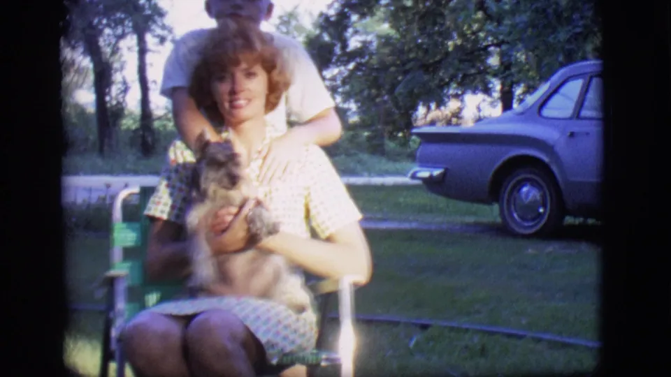 In the final 1966 Des Moines frame, the seated woman holds the small dog as a man stands close behind her and a car is visible across the lawn.