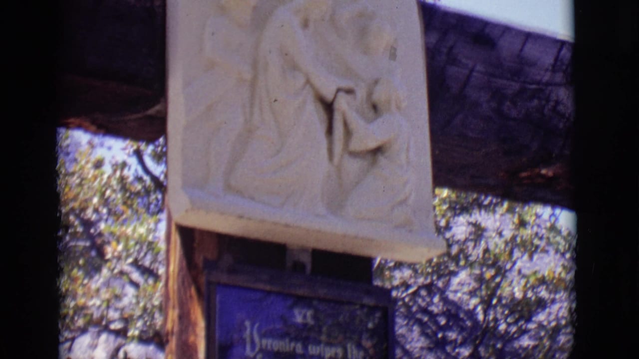 Carved relief above a blue religious plaque on a wooden post among trees.
