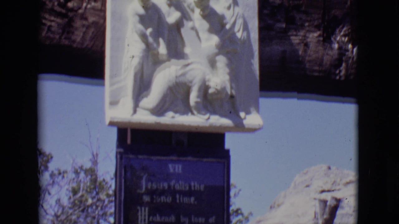 1965 San Luis, Colorado frame with the top of a devotional plaque and a white relief sculpture against sky and rock.
