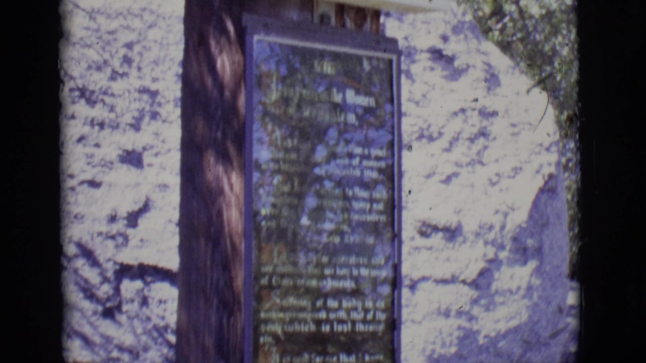 Close view of a dark religious plaque mounted beside a wooden post against pale rock.