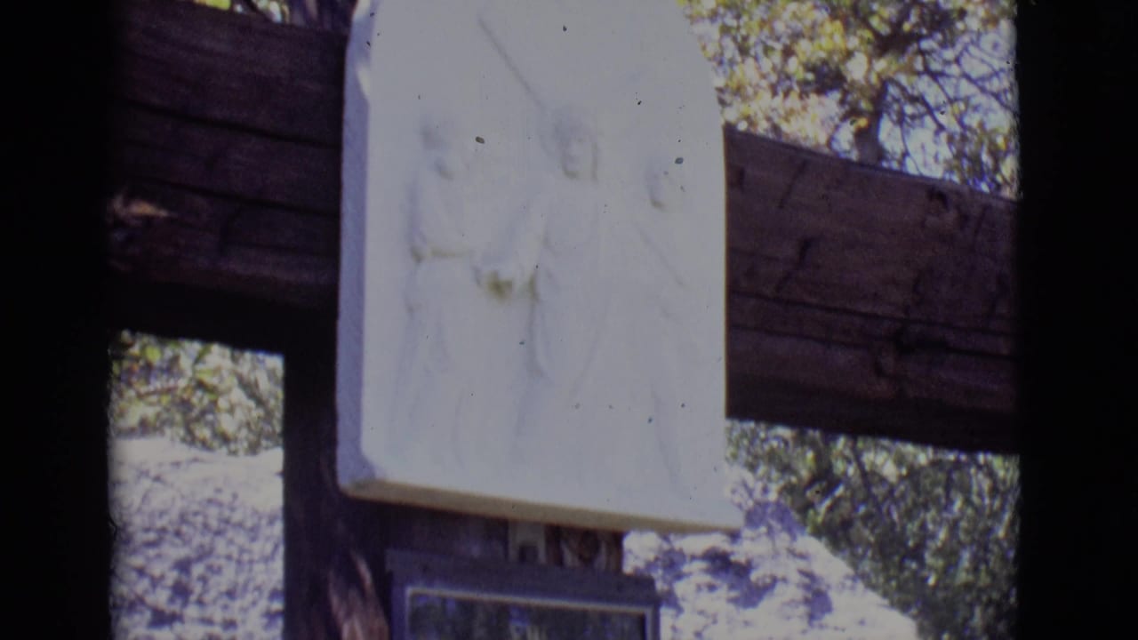 White religious relief mounted above a plaque on a wooden outdoor structure.