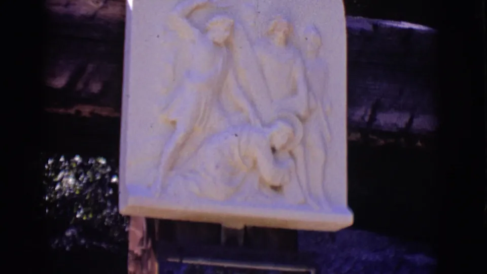 Close 1965 home-movie view of a pale carved Stations of the Cross relief, with figures around Jesus and the Ninth Station plaque partly below.