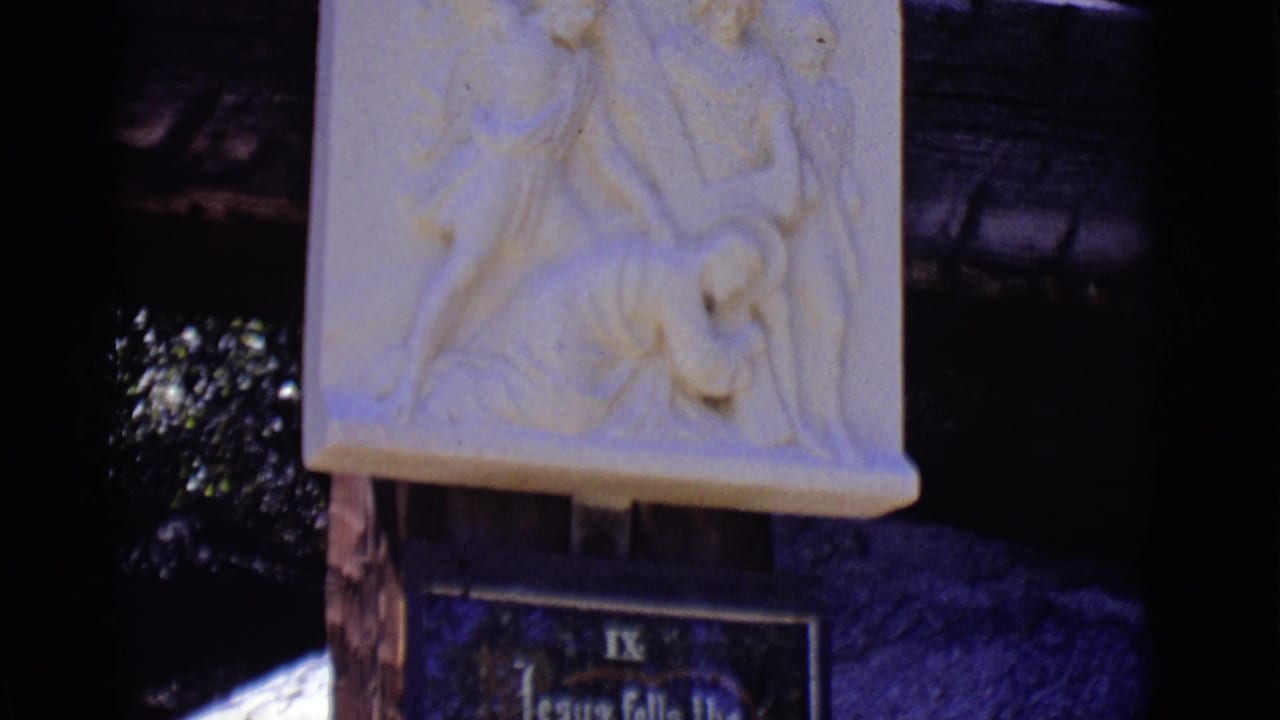 Carved relief above a blue plaque on a wooden post in outdoor shade.