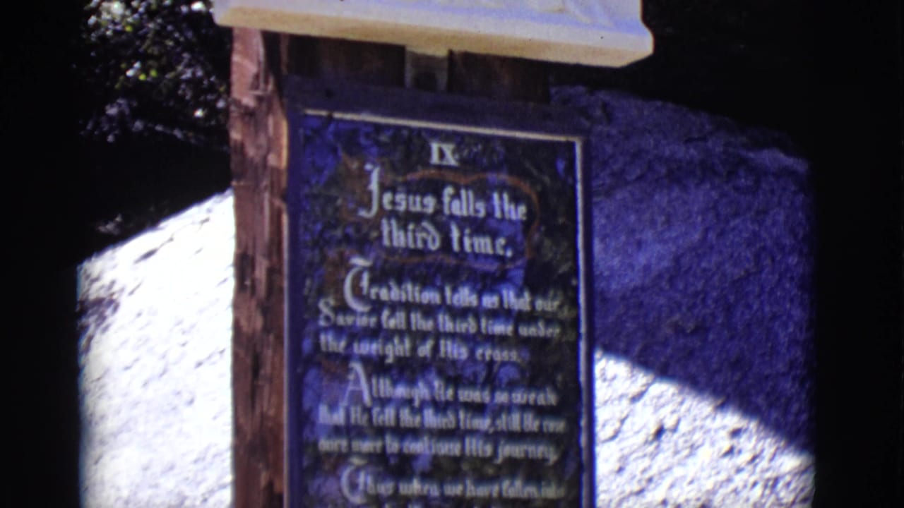 Blue plaque reading Jesus falls the third time beneath a pale relief panel.
