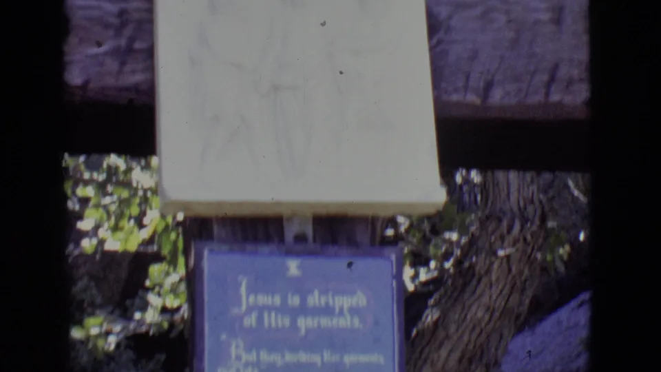 1965 San Luis, Colorado frame showing the lower relief panel above a blue plaque at an outdoor Stations of the Cross display.