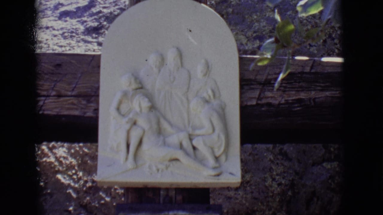 White religious relief mounted above a rough stone wall with leaves near the top edge.
