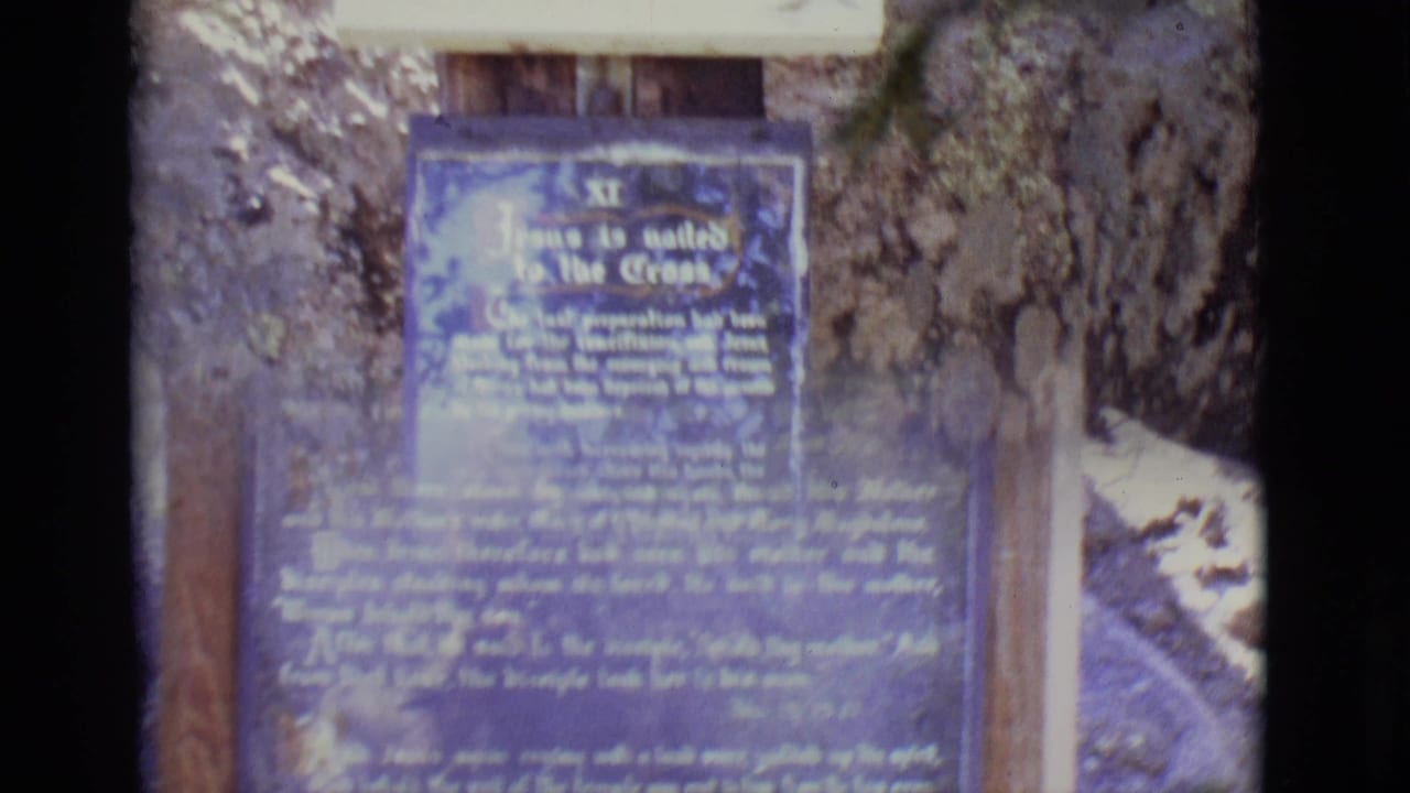 Weathered blue religious text sign mounted on wooden posts near stone and rock surfaces.