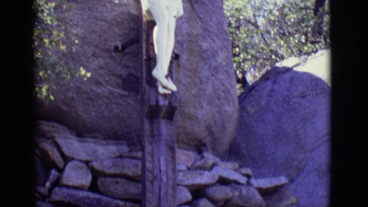 Partial crucifix statue beside large boulders and a low stone wall.