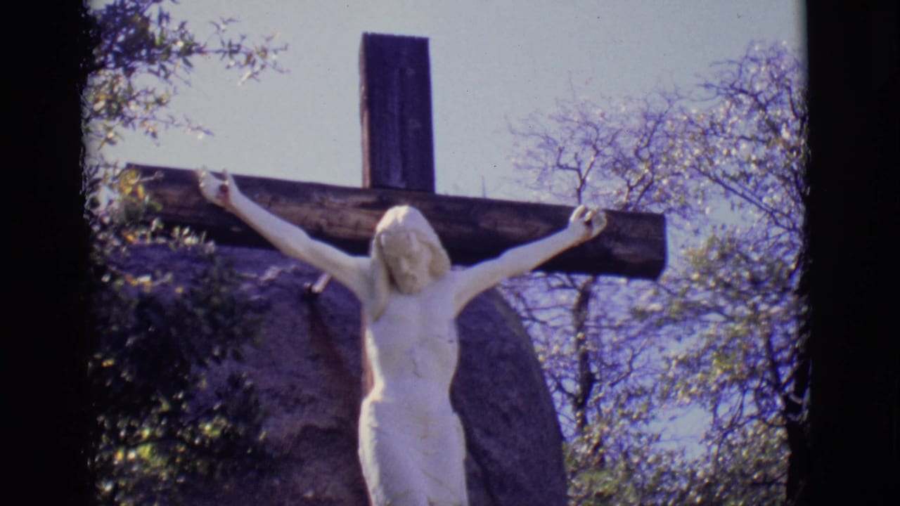 White crucifix statue outdoors against trees and pale sky.