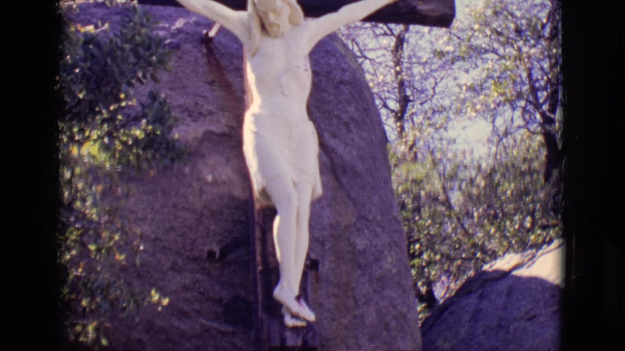Lower view of the crucifixion statue with rock and trees behind it.
