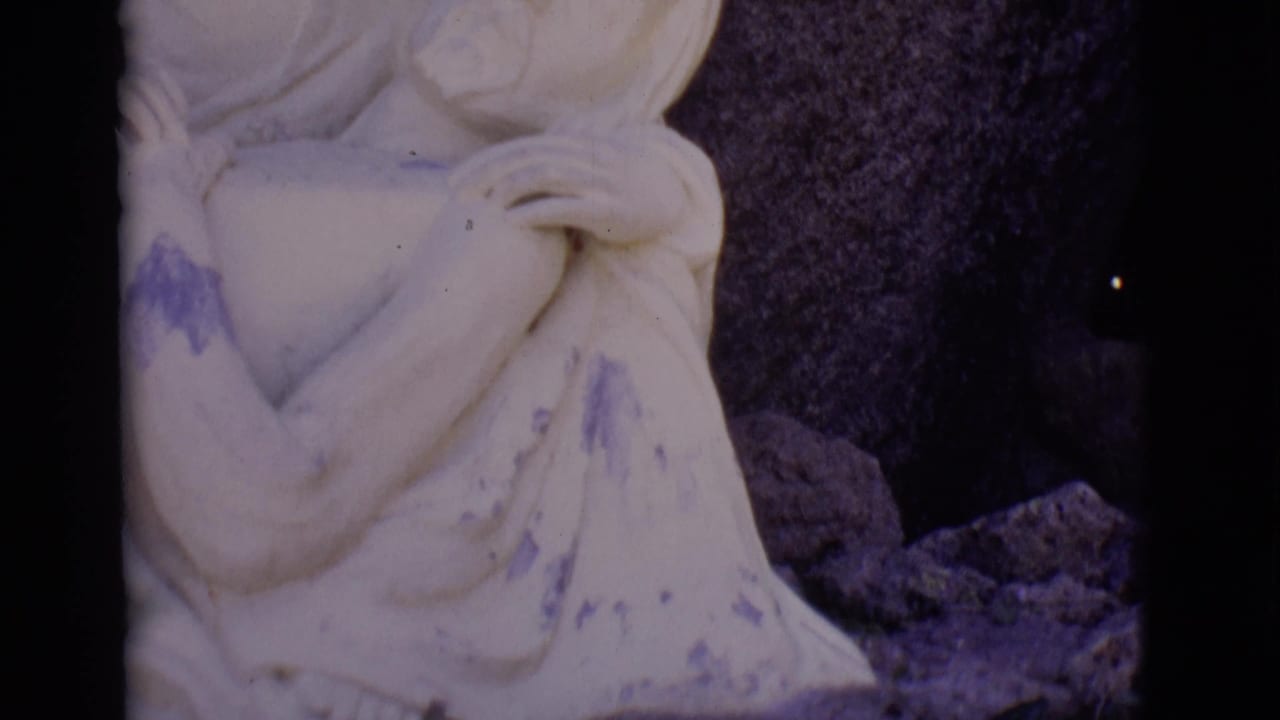 Close crop of pale stone Mary holding Jesus against a dark rock background.