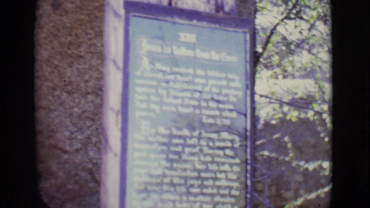 Blue religious plaque mounted beside stonework with foliage in the background.