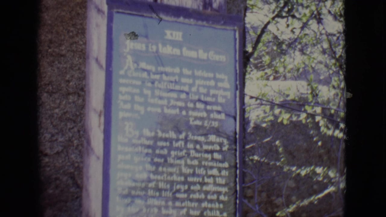 Weathered plaque beside trees with partially readable religious text.