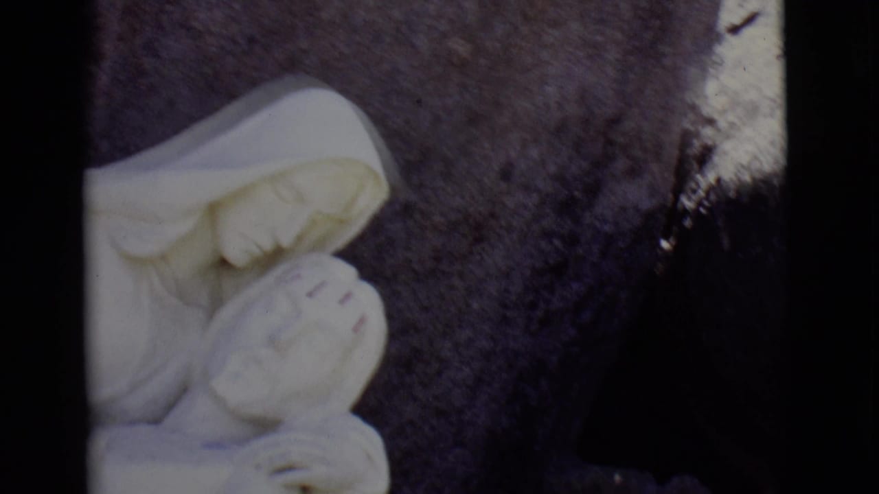 1965 San Luis, Colorado 8mm frame with a white marble Virgin Mary figure cradling Jesus against a dark stone backdrop.