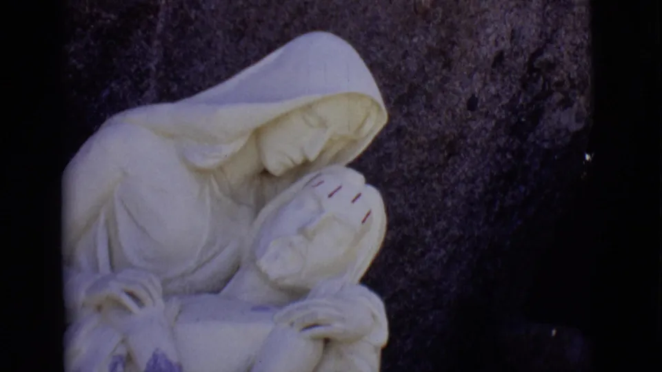 Close 1965 San Luis, Colorado 8mm view of the white marble Mary and Jesus sculpture, with robe folds and carved hands visible.